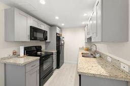 kitchen with light hardwood / wood-style floors, sink, light stone counters, and black appliances