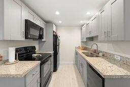 kitchen featuring white cabinets, light stone countertops, sink, and black appliances