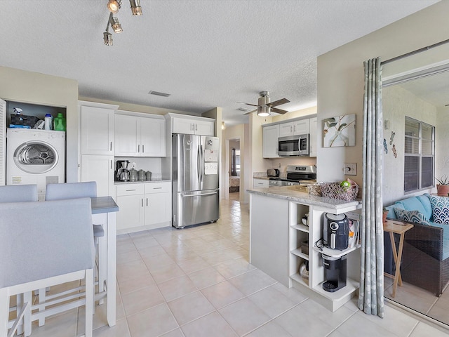 kitchen featuring stainless steel appliances, white cabinets, washer / clothes dryer, a textured ceiling, and light tile patterned floors