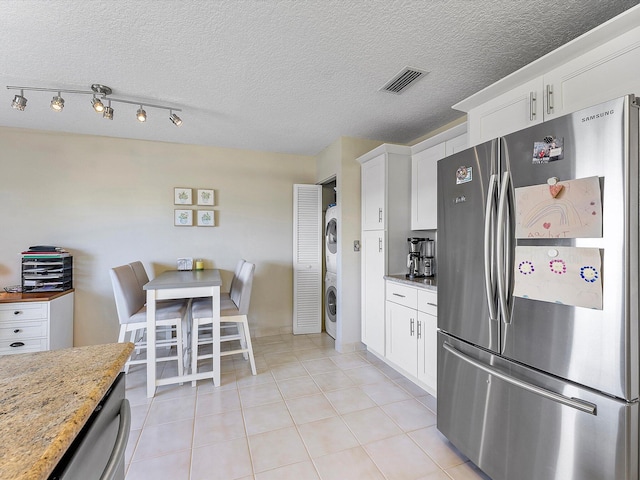 kitchen featuring white cabinets, stacked washer / drying machine, light stone countertops, and stainless steel refrigerator