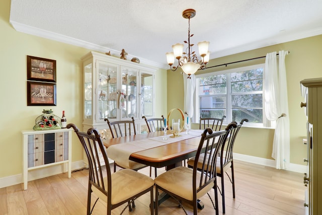 dining space with a textured ceiling, light hardwood / wood-style floors, crown molding, and an inviting chandelier