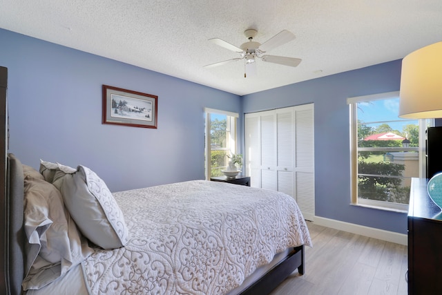 bedroom with ceiling fan, light hardwood / wood-style floors, a textured ceiling, and a closet