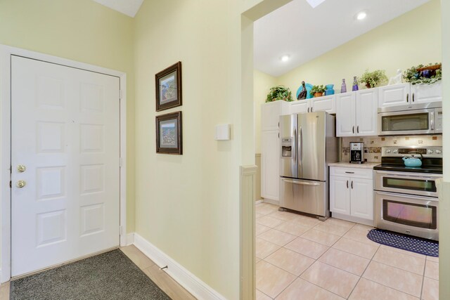 kitchen featuring lofted ceiling, white cabinets, appliances with stainless steel finishes, tasteful backsplash, and light tile patterned flooring