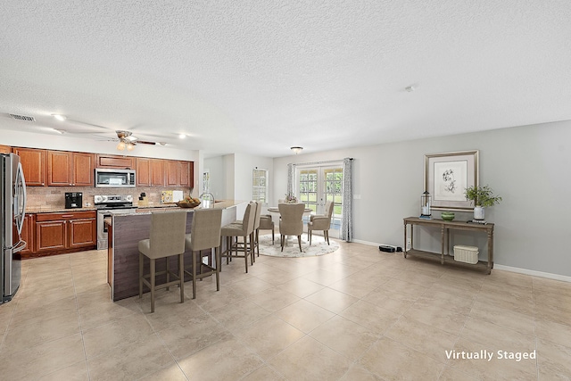 kitchen with tasteful backsplash, visible vents, a breakfast bar, an island with sink, and appliances with stainless steel finishes