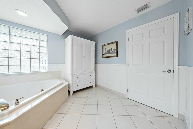 full bath featuring tile patterned floors, visible vents, wainscoting, and a tub with jets