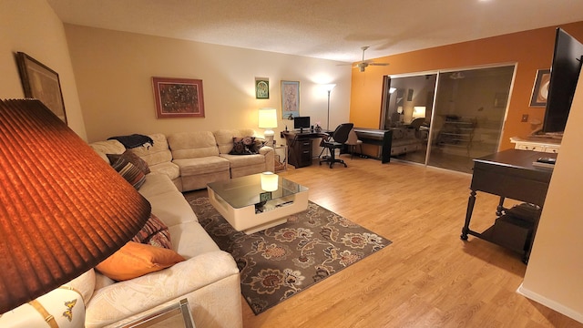 living room featuring ceiling fan, light wood-type flooring, and a textured ceiling