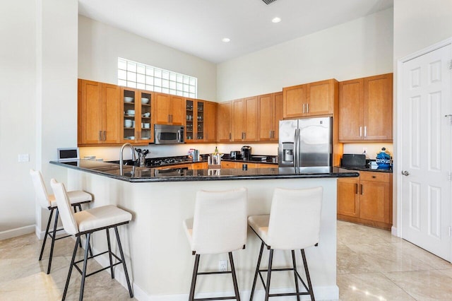 kitchen with kitchen peninsula, a towering ceiling, dark stone counters, a breakfast bar area, and appliances with stainless steel finishes