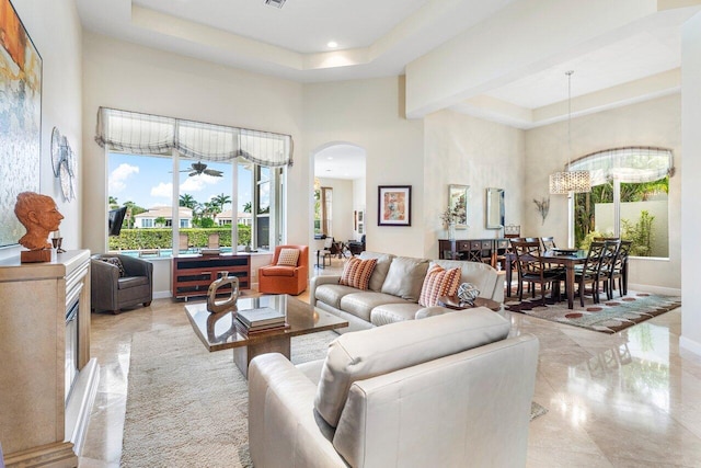 living room with a high ceiling, ceiling fan with notable chandelier, a tray ceiling, and a healthy amount of sunlight