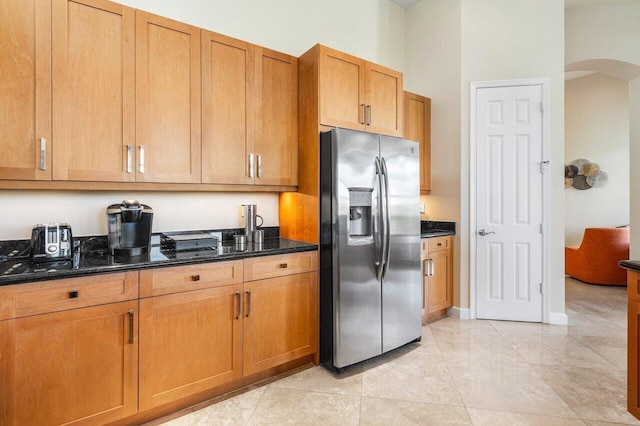 kitchen with stainless steel fridge, light tile patterned floors, and dark stone countertops