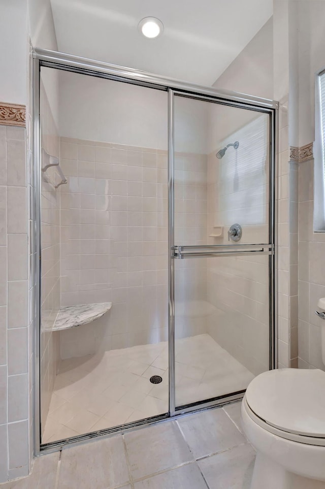 bathroom with tile patterned floors, toilet, and a shower with door