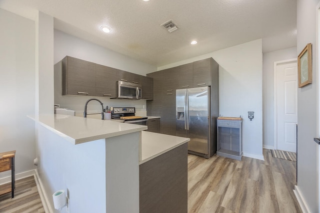 kitchen featuring sink, light hardwood / wood-style flooring, a textured ceiling, kitchen peninsula, and stainless steel appliances