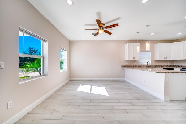 kitchen with light stone countertops, white cabinetry, ceiling fan, light hardwood / wood-style flooring, and pendant lighting