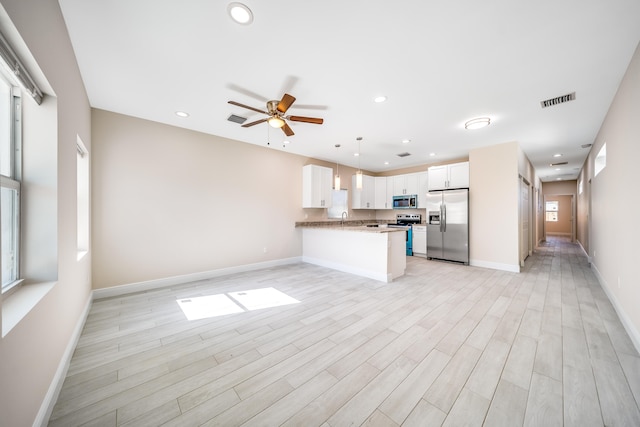 kitchen with white cabinets, hanging light fixtures, appliances with stainless steel finishes, light hardwood / wood-style floors, and kitchen peninsula