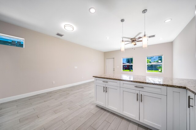 kitchen featuring light wood-type flooring, light stone counters, ceiling fan, decorative light fixtures, and white cabinetry