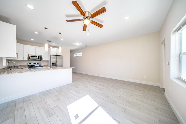 kitchen with light wood-type flooring, appliances with stainless steel finishes, decorative light fixtures, light stone counters, and white cabinetry