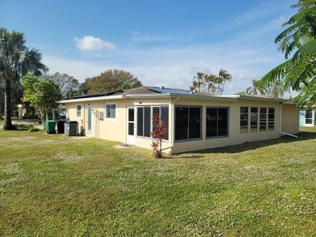 back of property with central air condition unit, a yard, and solar panels