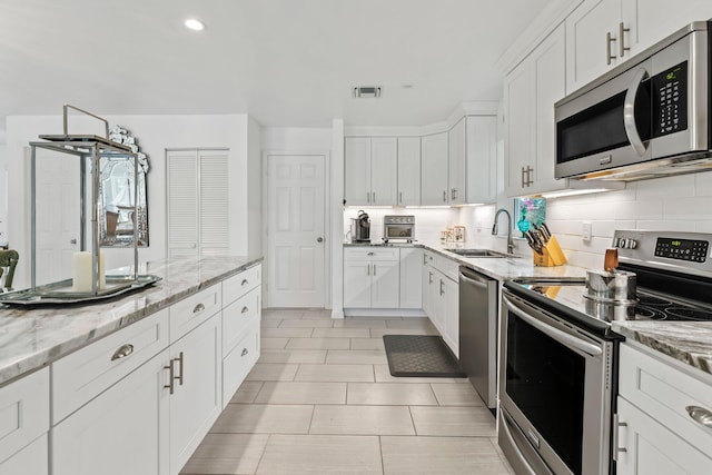 kitchen with backsplash, white cabinets, sink, light stone countertops, and stainless steel appliances