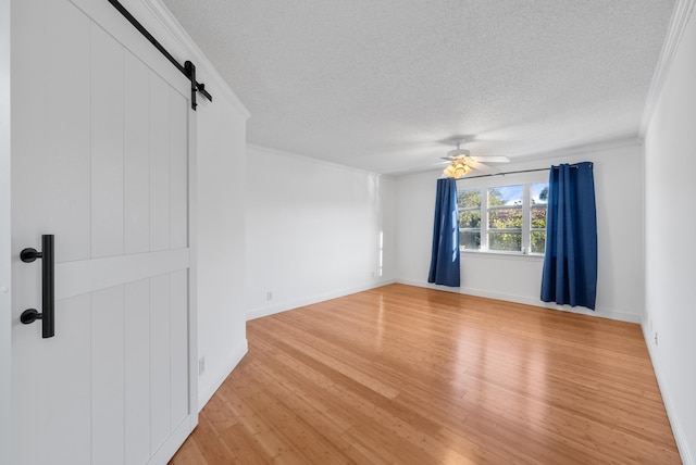 empty room with crown molding, ceiling fan, a textured ceiling, a barn door, and light wood-type flooring