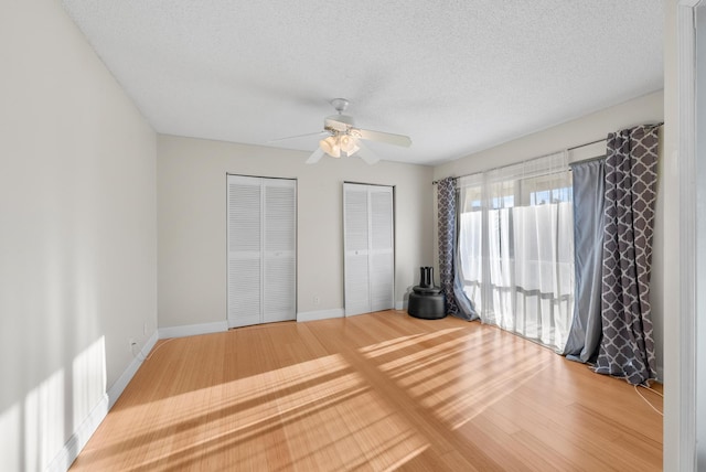 unfurnished bedroom featuring ceiling fan, two closets, a textured ceiling, and hardwood / wood-style flooring