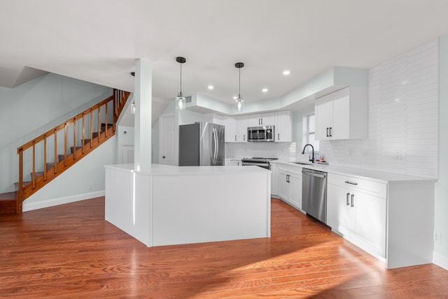 kitchen featuring sink, a kitchen island, wood-type flooring, white cabinets, and appliances with stainless steel finishes