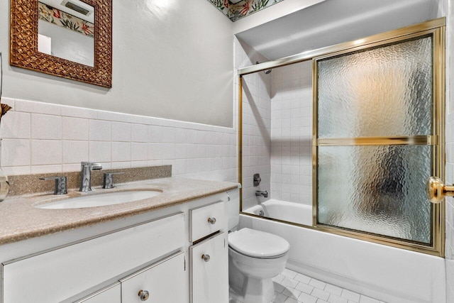 full bathroom with bath / shower combo with glass door, vanity, tile walls, tile patterned flooring, and toilet