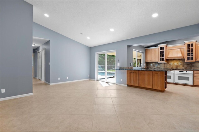 kitchen featuring premium range hood, oven, dark stone counters, vaulted ceiling, and light tile patterned floors