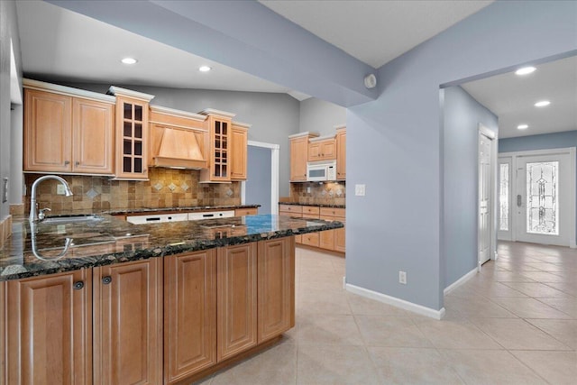 kitchen with kitchen peninsula, dark stone counters, custom range hood, vaulted ceiling, and sink