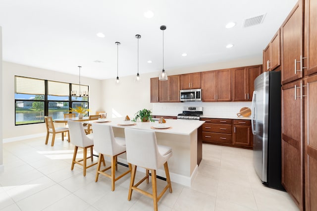 kitchen featuring decorative backsplash, appliances with stainless steel finishes, a kitchen breakfast bar, a kitchen island, and hanging light fixtures