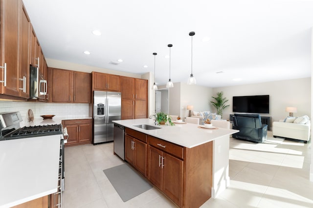 kitchen with sink, hanging light fixtures, stainless steel appliances, tasteful backsplash, and a center island with sink