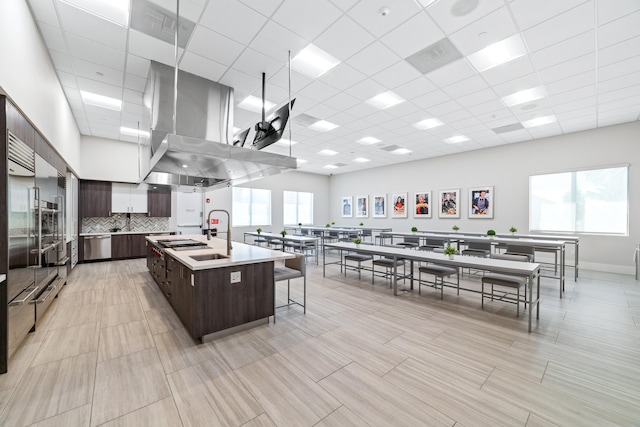 kitchen with a drop ceiling, sink, a kitchen bar, a kitchen island with sink, and dark brown cabinets