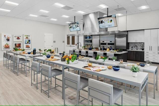 kitchen featuring a paneled ceiling, light hardwood / wood-style flooring, stainless steel built in fridge, and a center island with sink