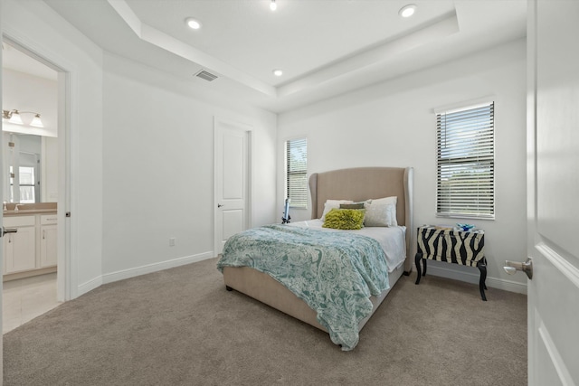 carpeted bedroom featuring a raised ceiling and ensuite bath