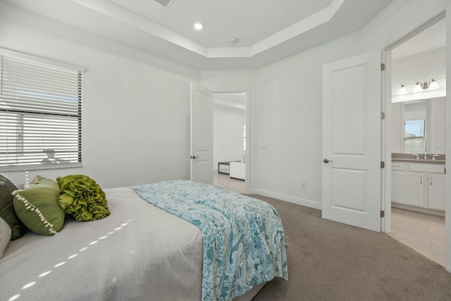 carpeted bedroom featuring sink, a tray ceiling, and ensuite bath