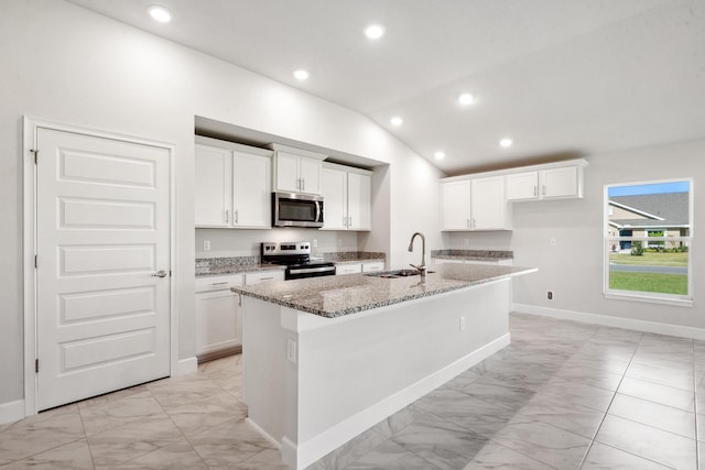 kitchen featuring light stone countertops, stainless steel appliances, vaulted ceiling, a kitchen island with sink, and sink