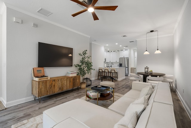 living room featuring hardwood / wood-style flooring, ceiling fan, ornamental molding, and sink