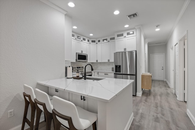 kitchen with sink, kitchen peninsula, light stone counters, white cabinetry, and stainless steel appliances