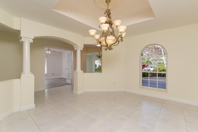 unfurnished room featuring ornate columns, ceiling fan with notable chandelier, light tile patterned floors, and a tray ceiling