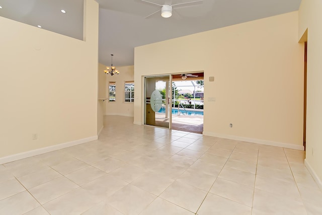 tiled spare room with a high ceiling and ceiling fan with notable chandelier