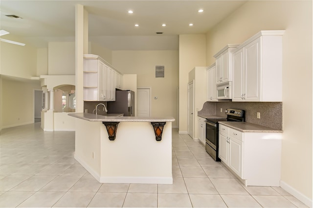 kitchen with light tile patterned floors, appliances with stainless steel finishes, white cabinetry, a towering ceiling, and a kitchen bar