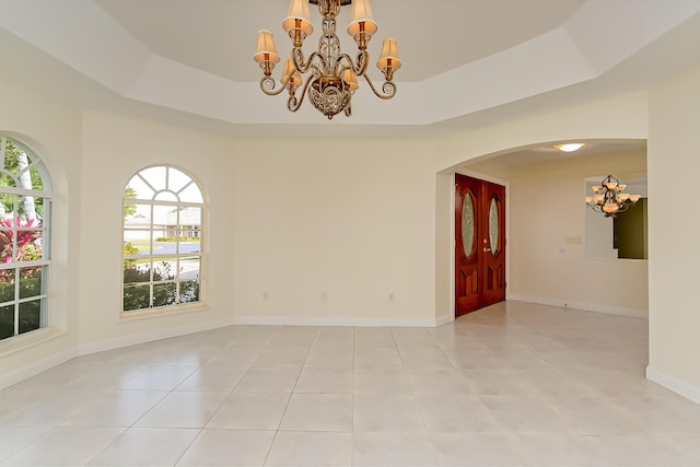 spare room with light tile patterned flooring, a chandelier, and a tray ceiling