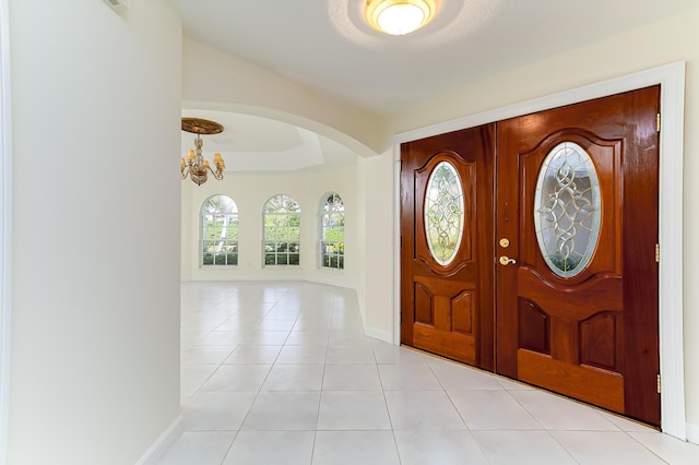 entrance foyer featuring an inviting chandelier, light tile patterned floors, and a tray ceiling