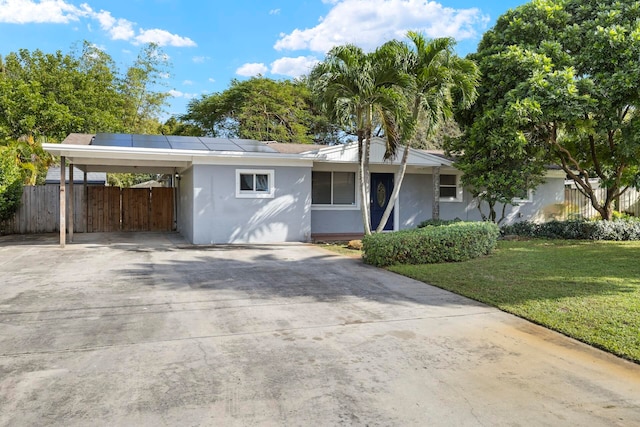 ranch-style home with a carport, solar panels, and a front yard