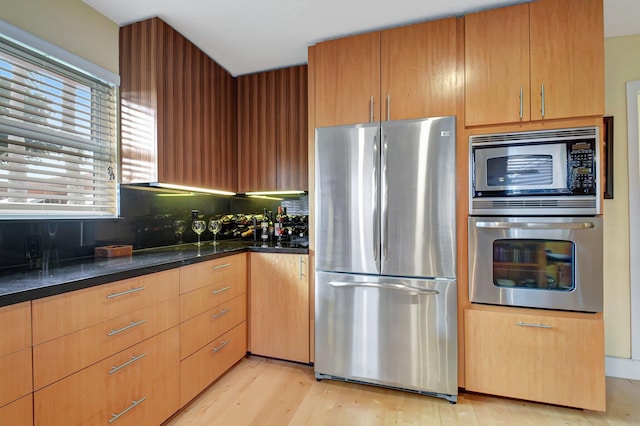 kitchen featuring decorative backsplash, dark stone countertops, stainless steel appliances, and light hardwood / wood-style flooring