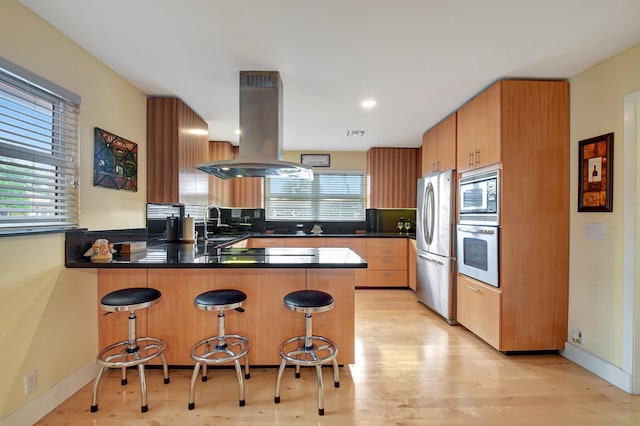 kitchen with a kitchen breakfast bar, island range hood, kitchen peninsula, and stainless steel appliances