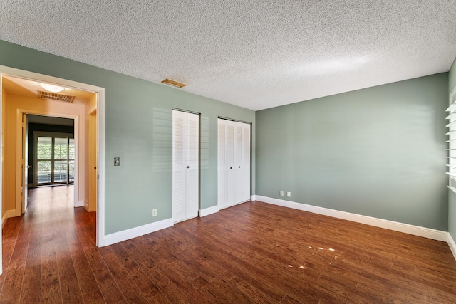 unfurnished bedroom with multiple closets, dark wood-type flooring, and a textured ceiling