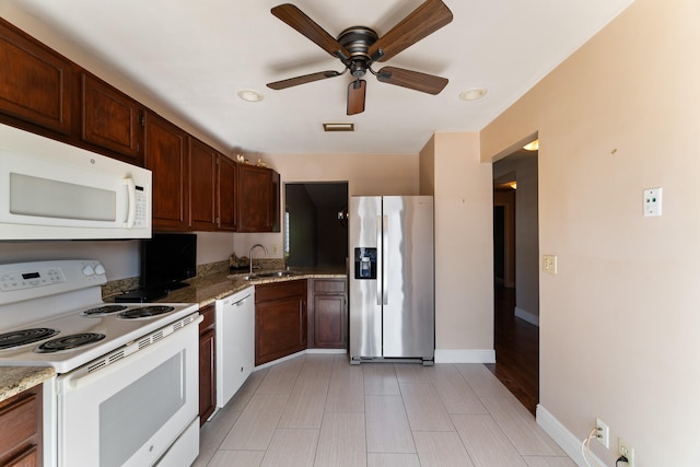 kitchen featuring white appliances, sink, ceiling fan, light stone countertops, and dark brown cabinets