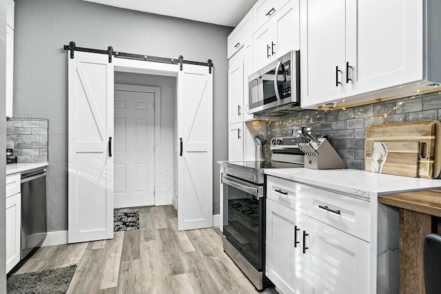 kitchen with white cabinets, a barn door, light wood-type flooring, and appliances with stainless steel finishes