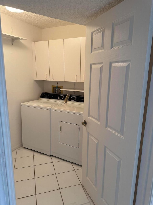 washroom featuring washing machine and clothes dryer, light tile patterned flooring, cabinets, and a textured ceiling