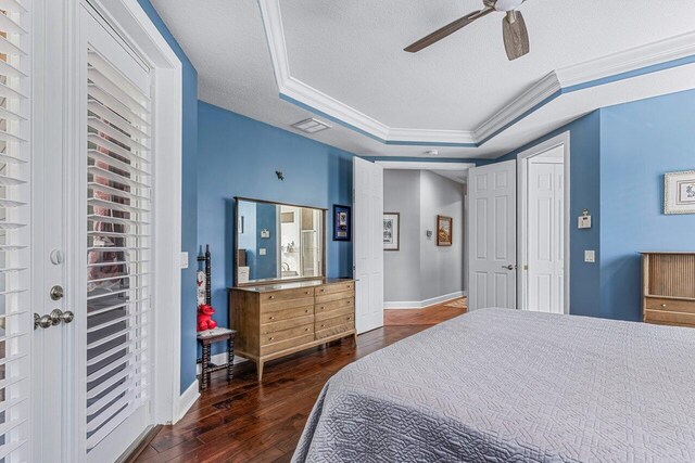 bedroom with dark wood-type flooring, a raised ceiling, ceiling fan, ornamental molding, and a textured ceiling