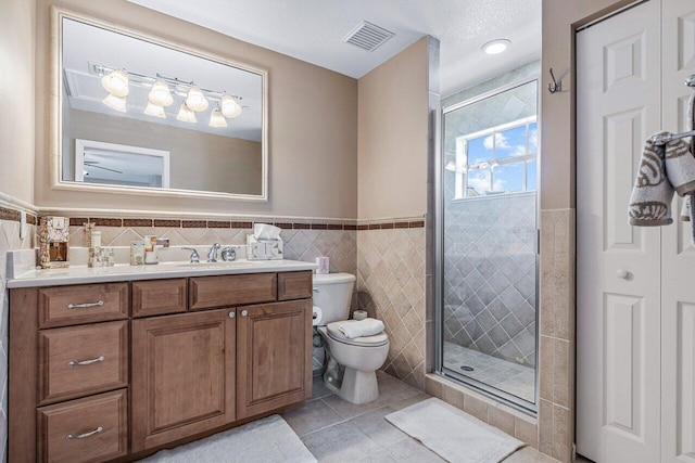 bathroom featuring tile patterned floors, an enclosed shower, toilet, vanity, and tile walls